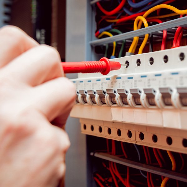 Hand holding test probe to test control panel circuit breaker